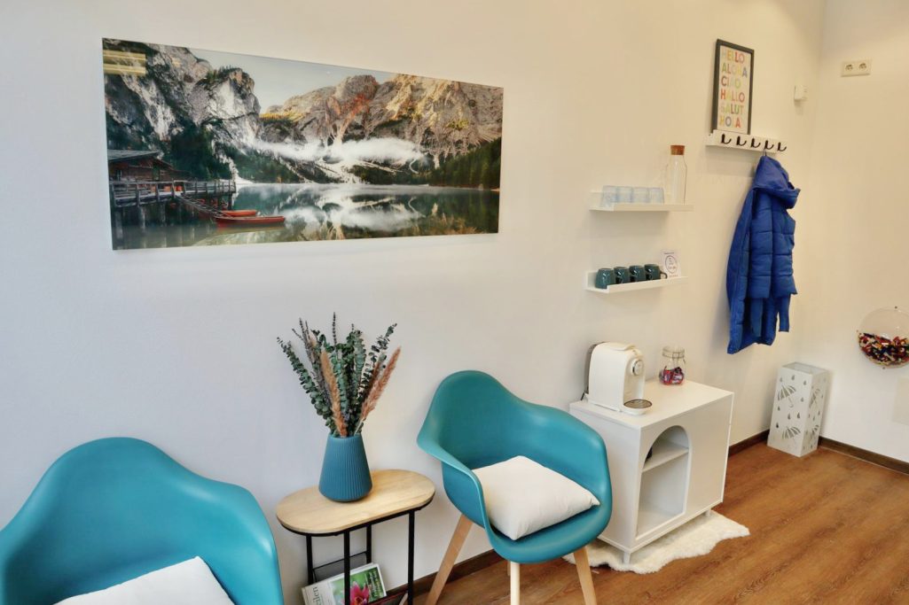 Wartezimmer Helle Praxis mit blauen Stühlen, Pflanzen und einem Bergbild an der Wand.